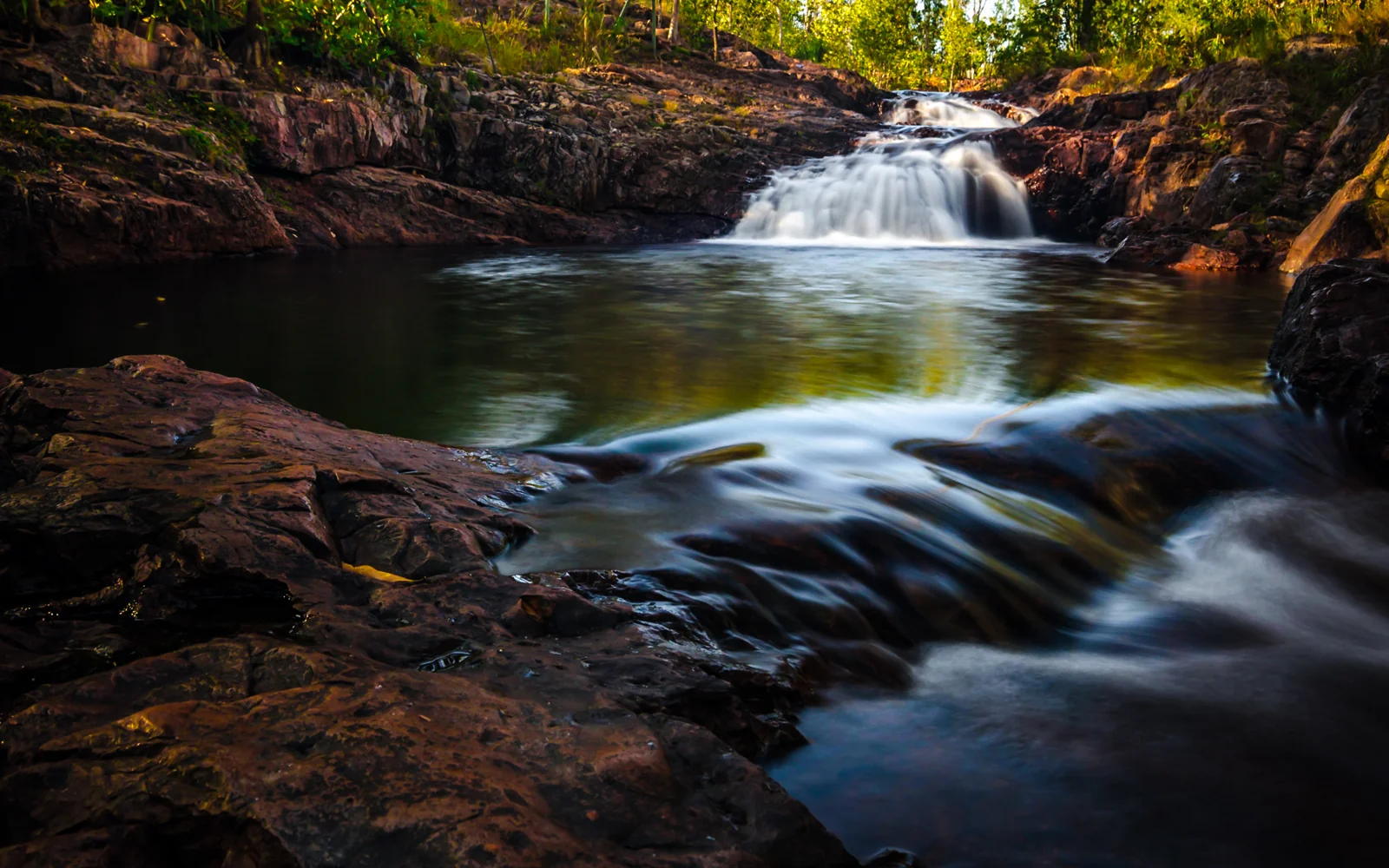 Waterfall flowing over dark rocks into a forest pool