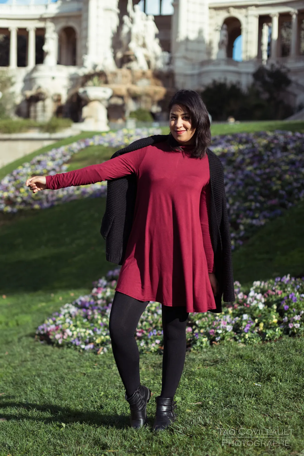 Woman in a burgundy dress standing on a lawn in front of an ornate building.