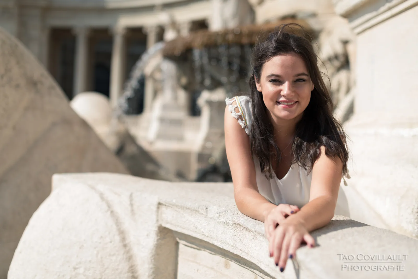 Woman in a white dress posing among pale stone columns.