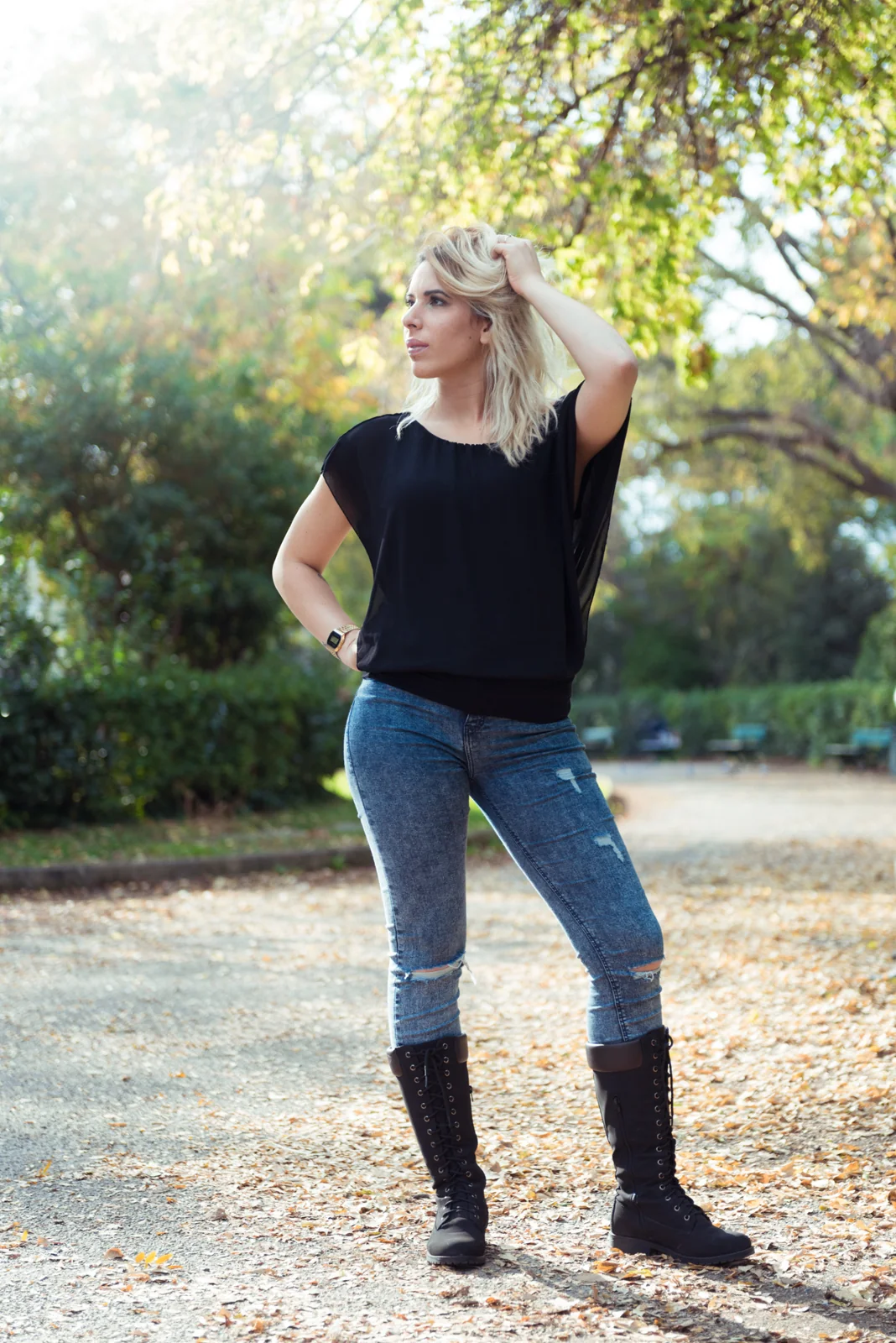 Woman in a black top and jeans posing in a leafy park.