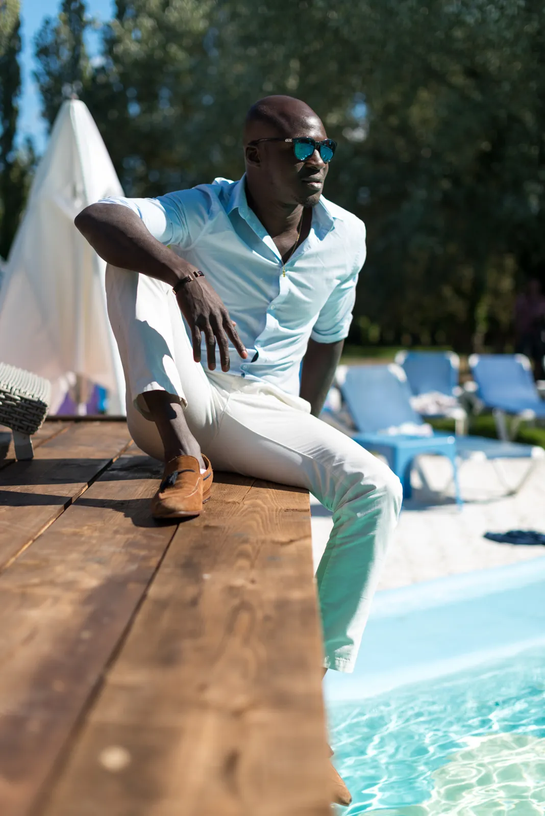 Man in a white shirt posing at the edge of a swimming pool.