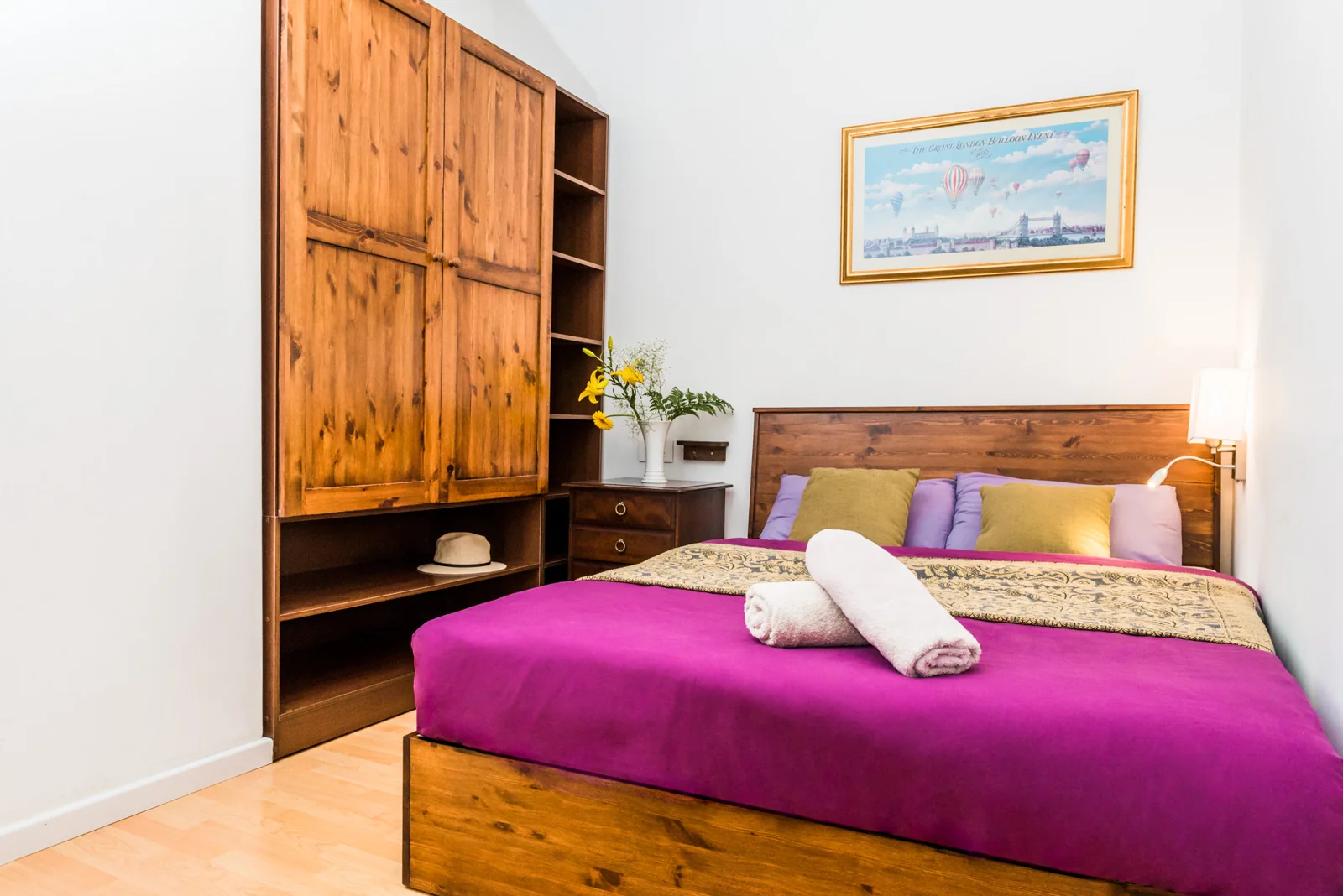 Bright bedroom with a magenta bedspread and wooden furniture.