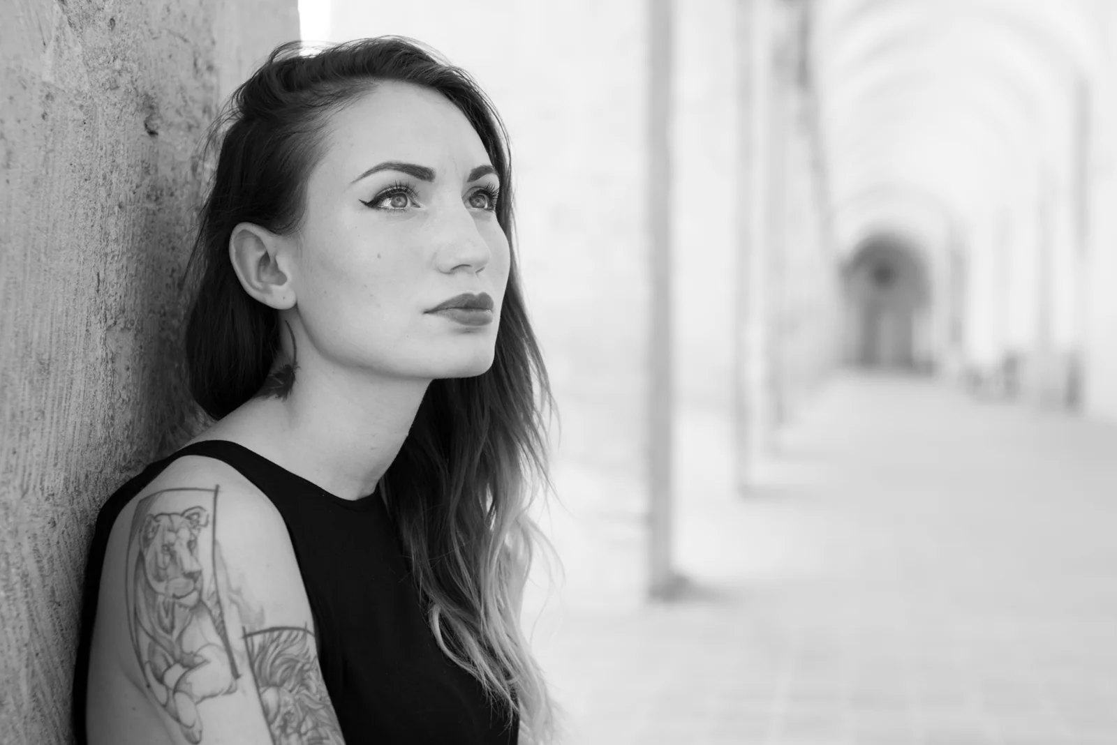 Black-and-white photograph: woman in black clothing posing in a stone arcade.
