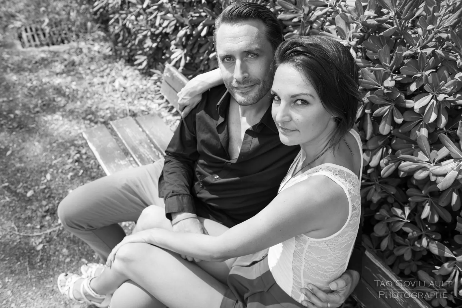 Black-and-white photograph: couple sitting together beneath trees.
