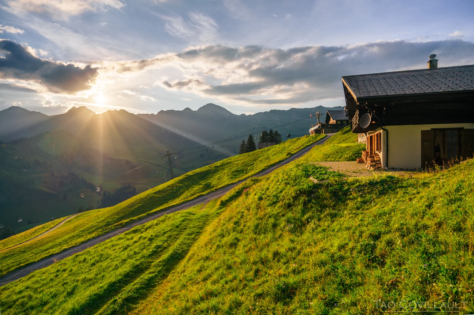 Mountain chalet on a grassy slope at sunset.
