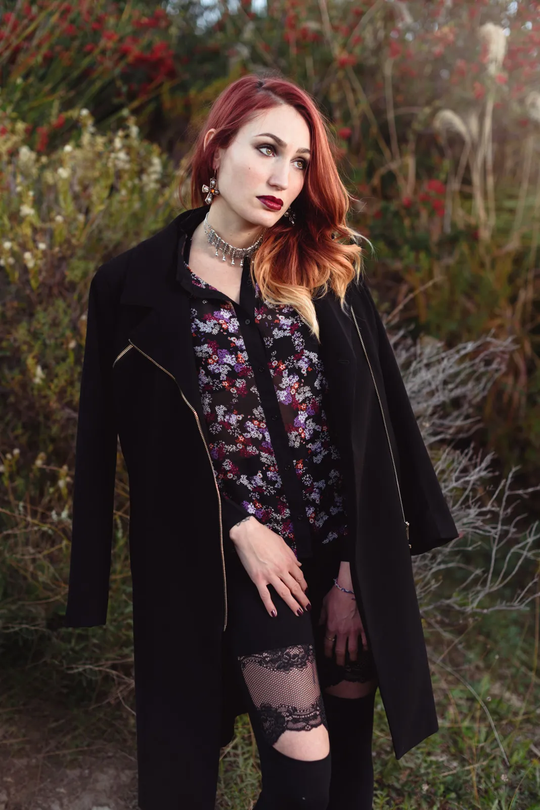 Red-haired woman standing beside flowering shrubs.
