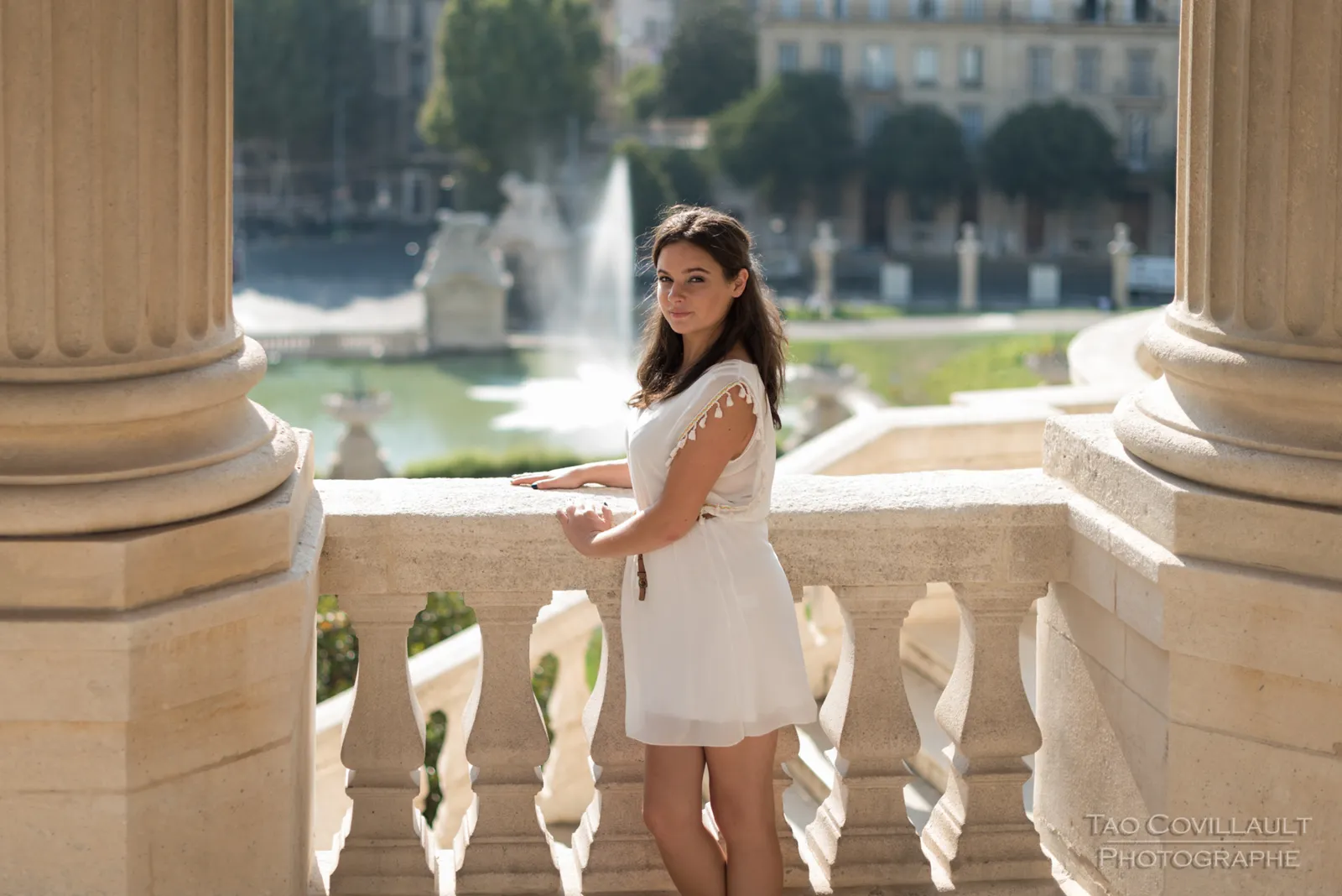Woman in a white dress posing on stone steps and beside a balustrade.