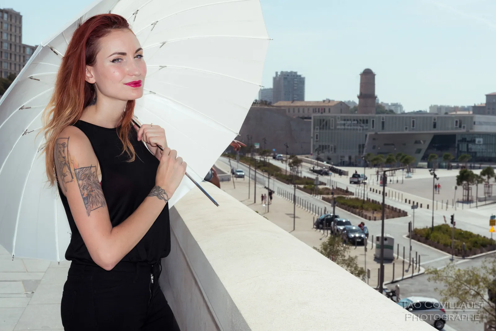 Woman in black clothing standing at a stone parapet overlooking the city.