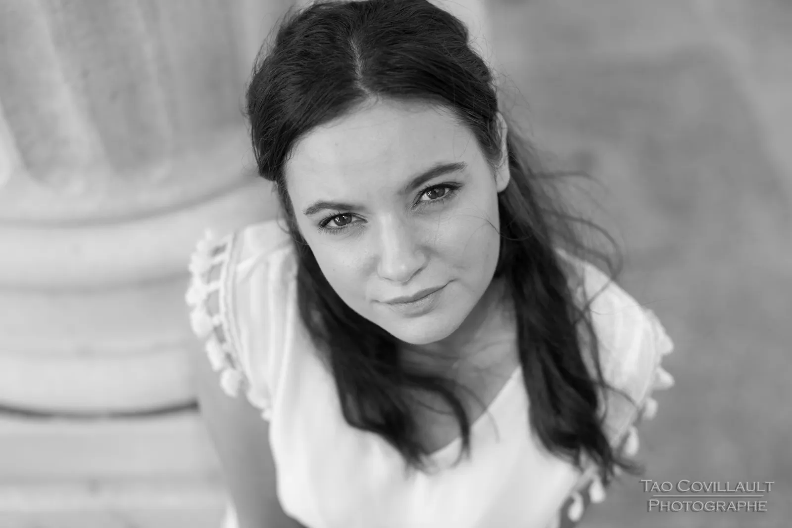 Black-and-white photograph: woman in a white dress posing among pale stone columns.