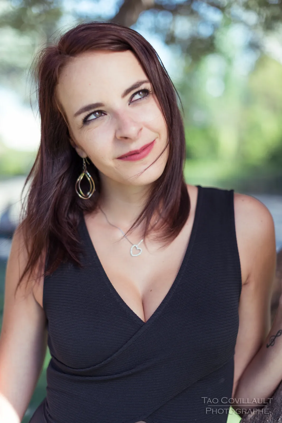 Woman in a black dress posing among trees.