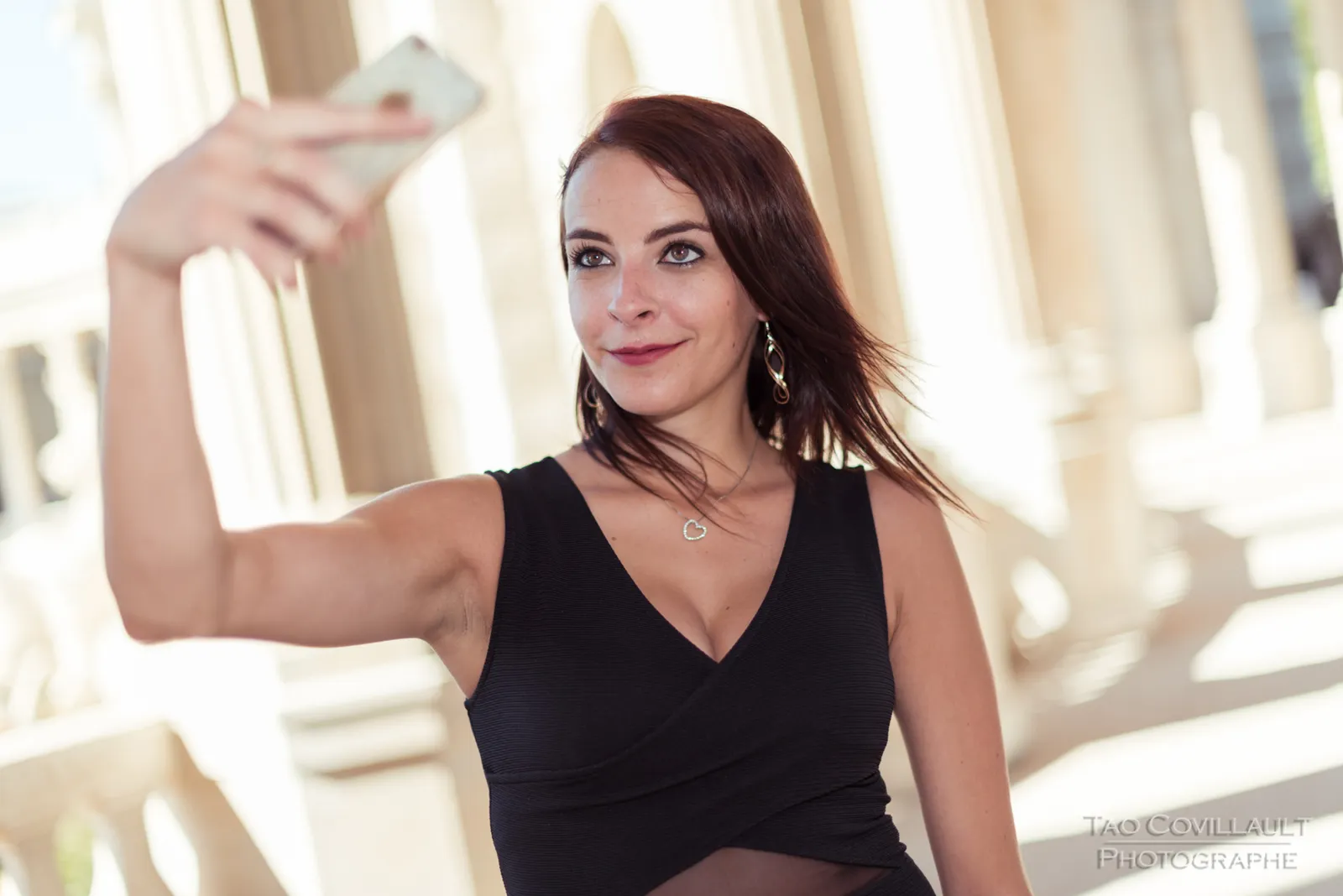 Woman in a black dress posing near pale stone columns.