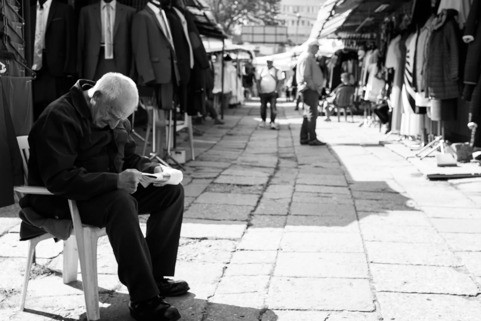 Seated person reading in a market passage in black and white