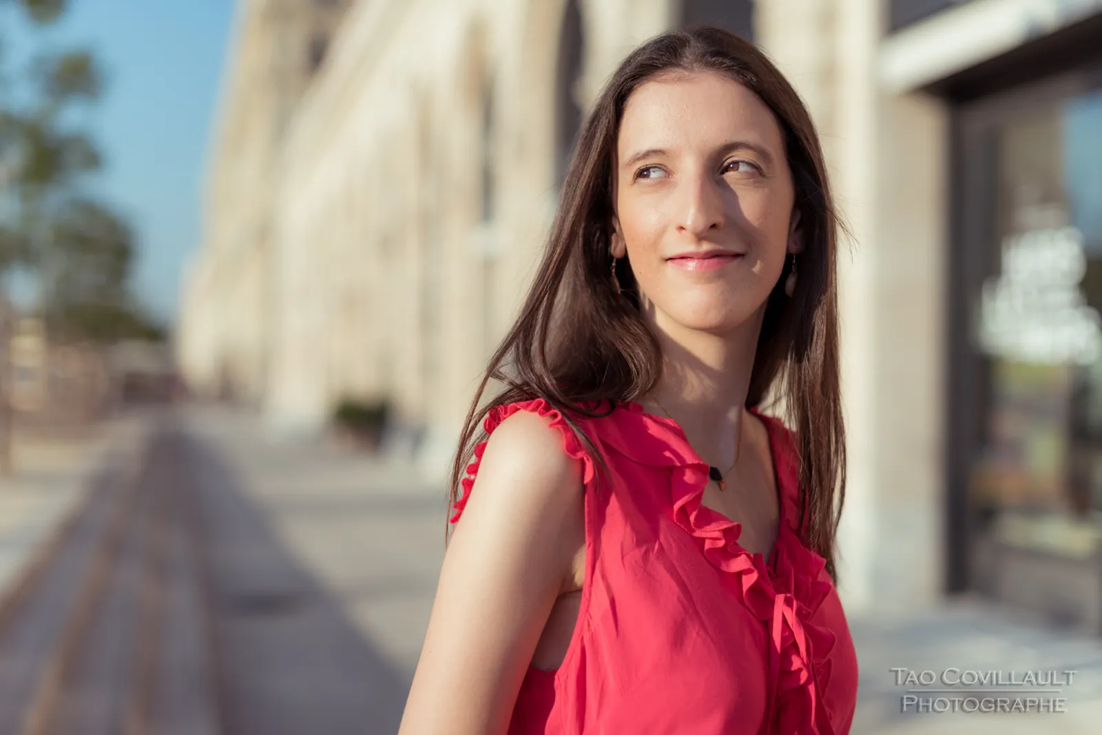 Woman in a bright pink top and patterned skirt posing beside stone steps and walls.