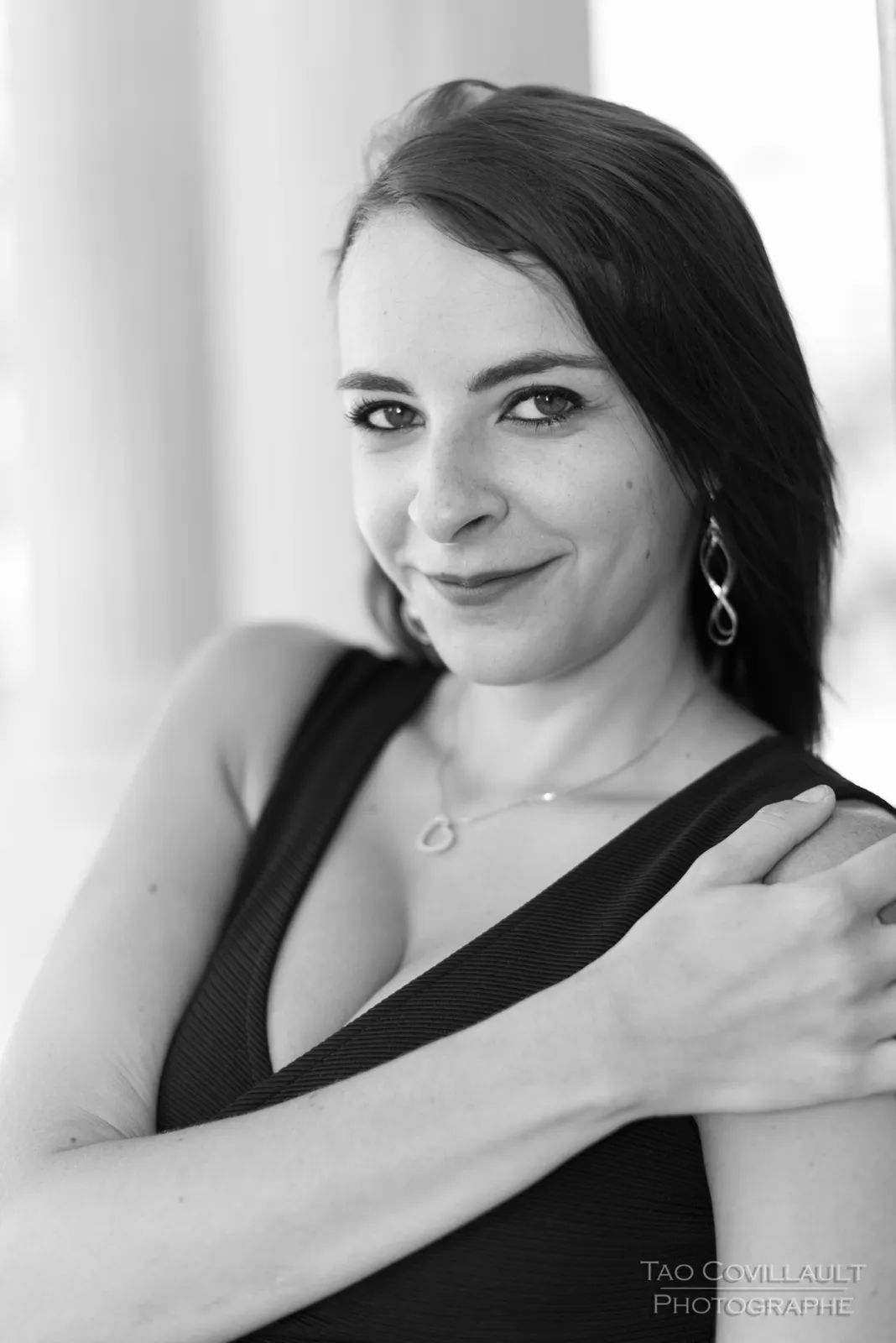 Black-and-white photograph: woman in a black dress posing near pale stone columns.