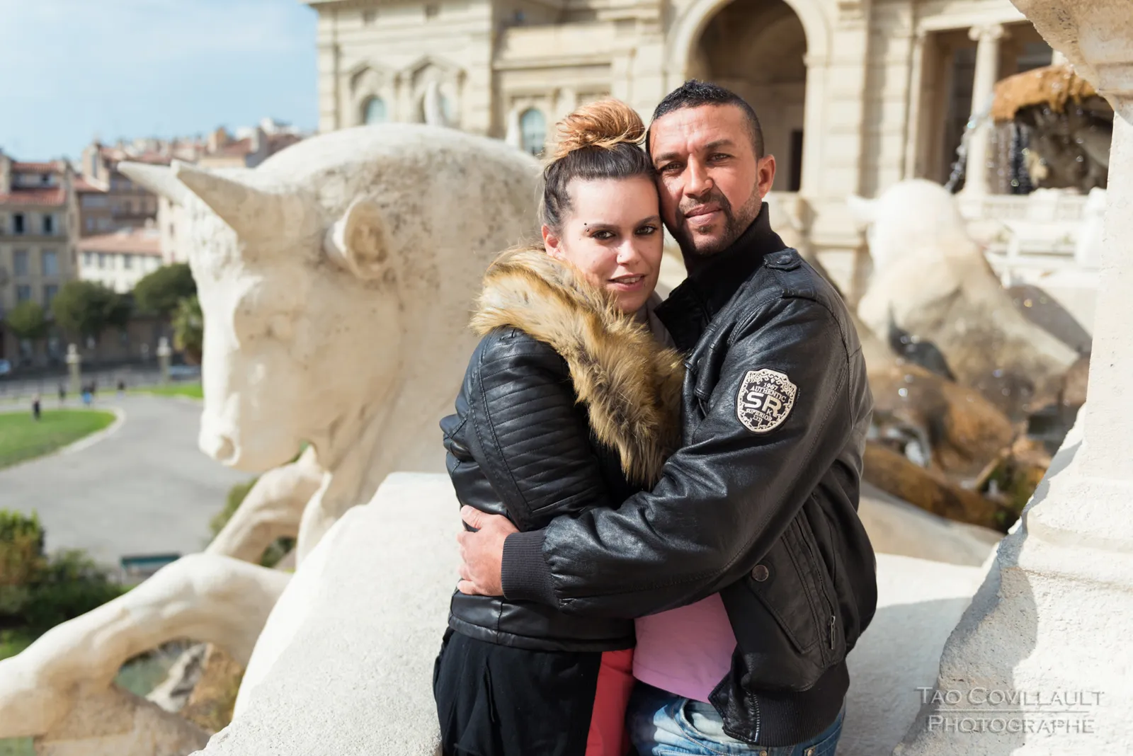 Couple embracing beside pale stone columns and sculptures.