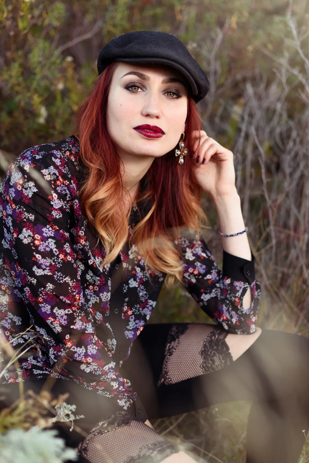 Red-haired woman in a hat posing beside a tree.