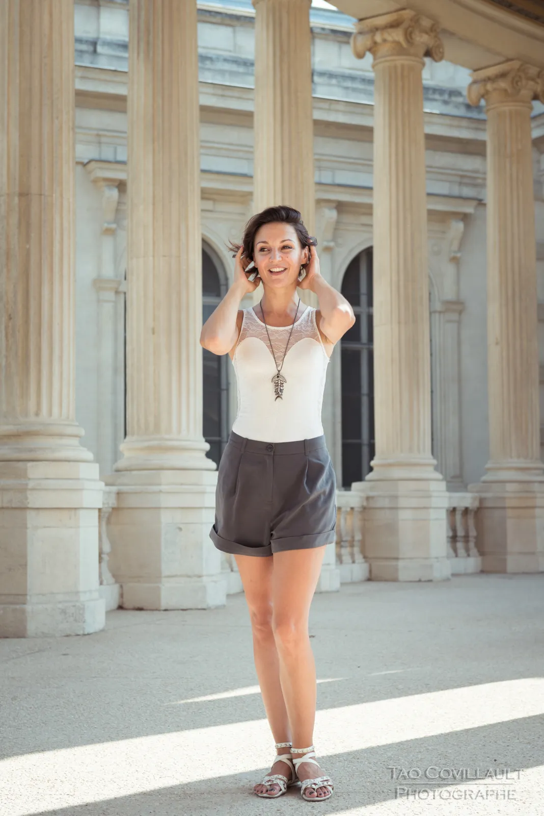 Woman in a white sleeveless top posing beside pale stone columns.