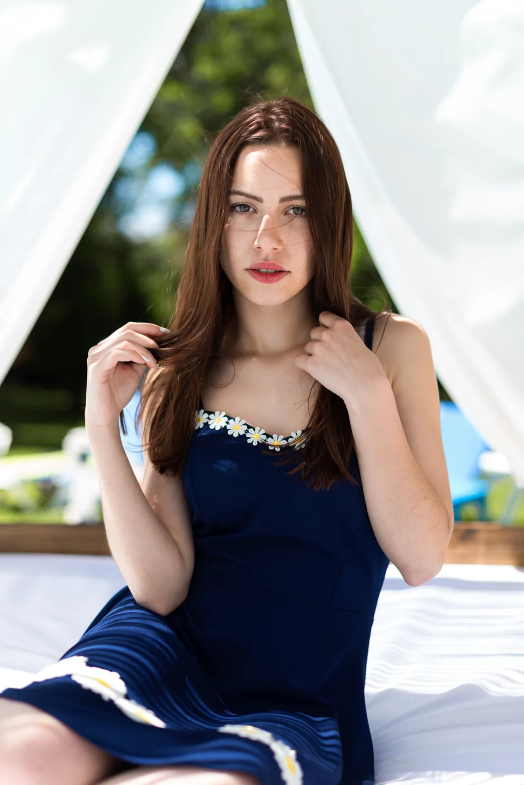Woman in a blue dress seated beneath poolside curtains.