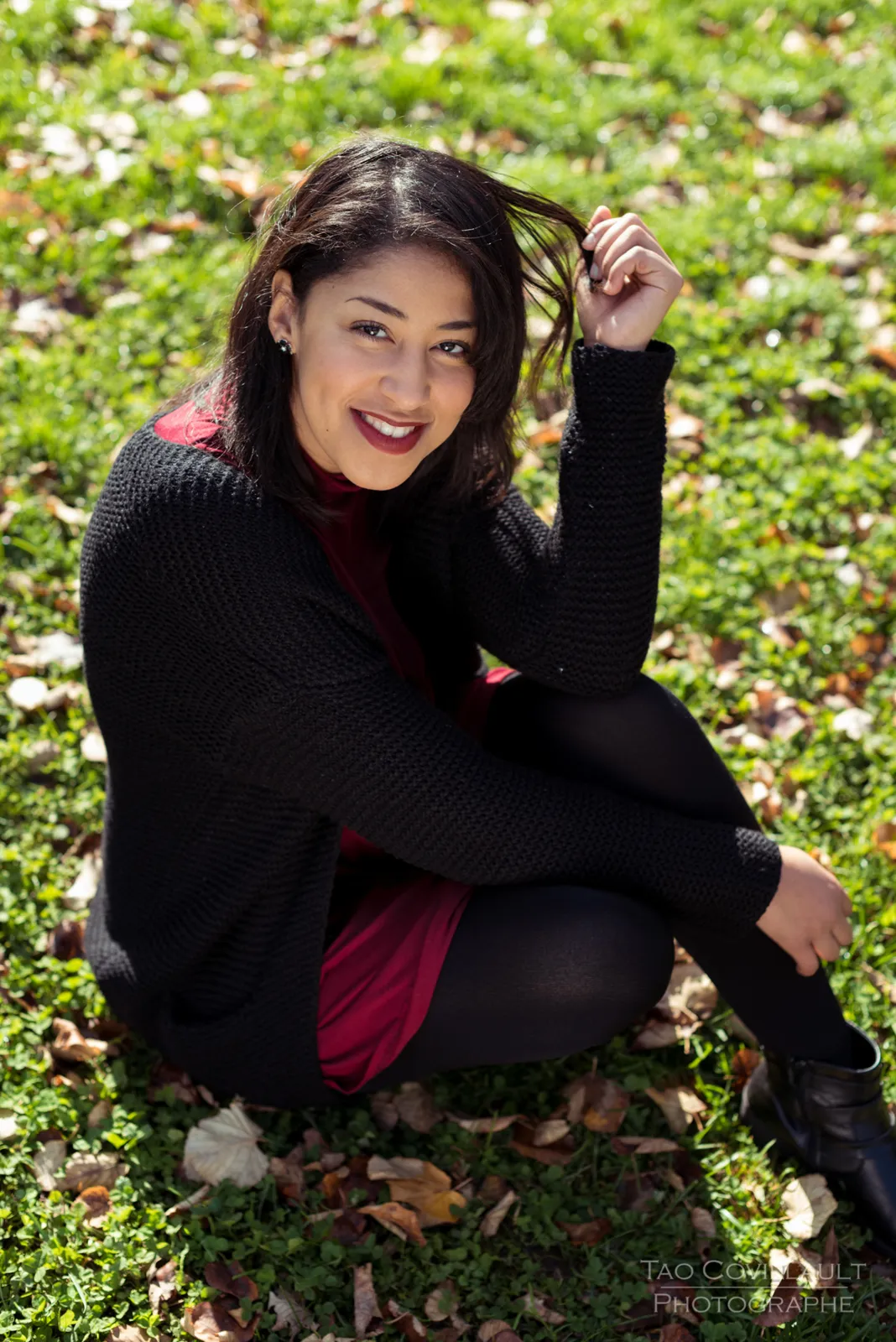 Woman in a burgundy dress and dark coat sitting among trees.