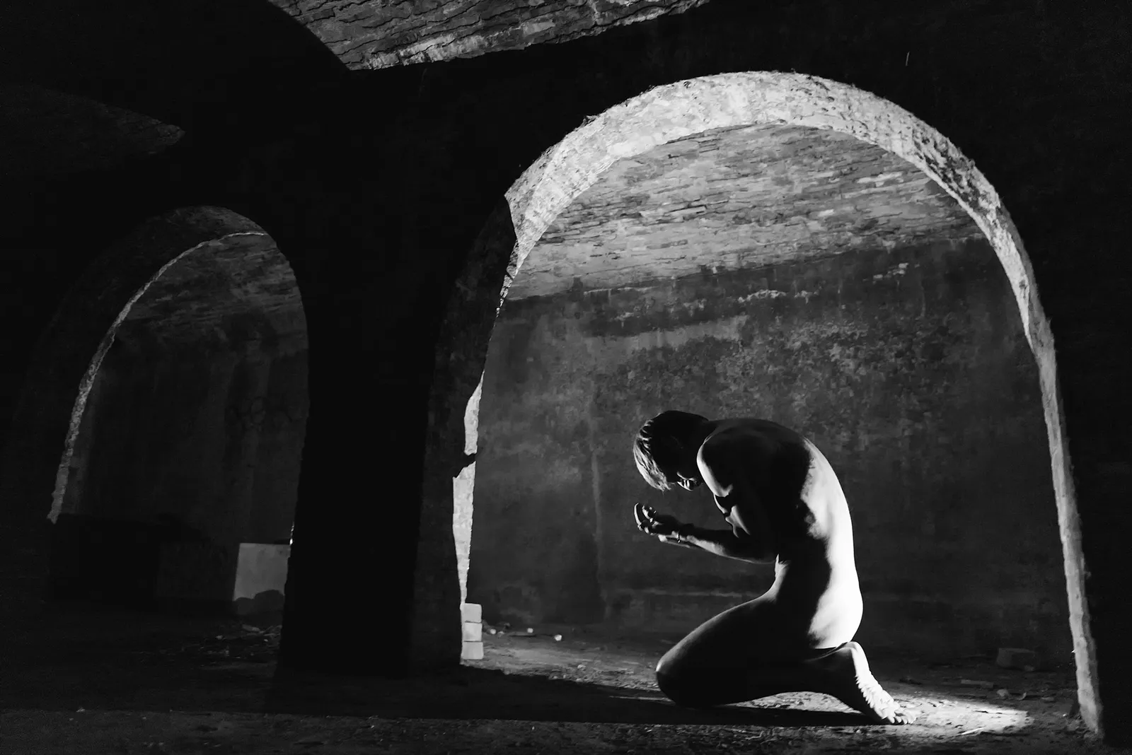Curled figure beneath a stone arch in black and white