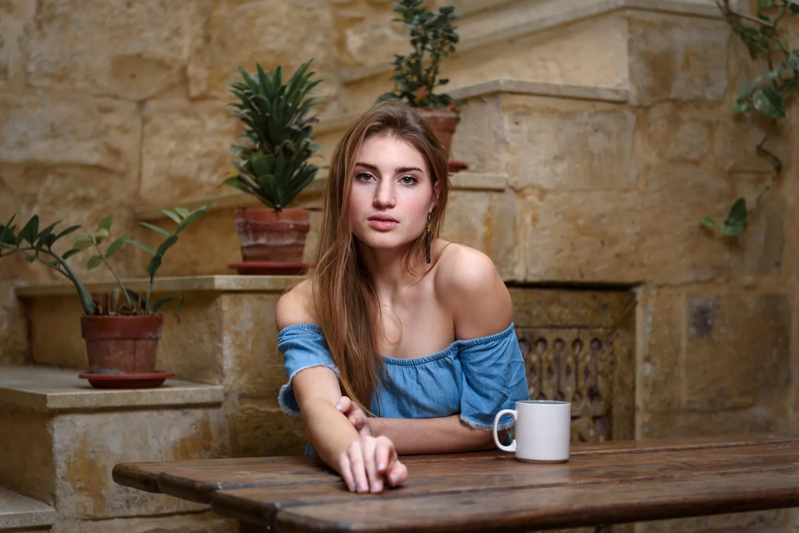 Woman in a blue top seated at a table beside a stone wall.
