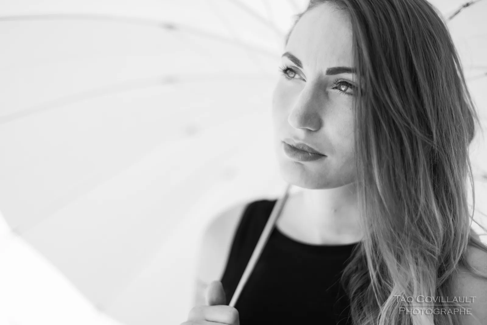 Black-and-white photograph: woman in black clothing holding a white parasol.