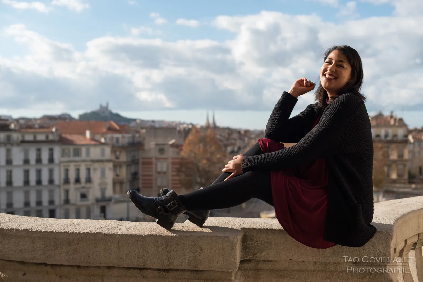 Woman seated on a stone parapet overlooking the city.