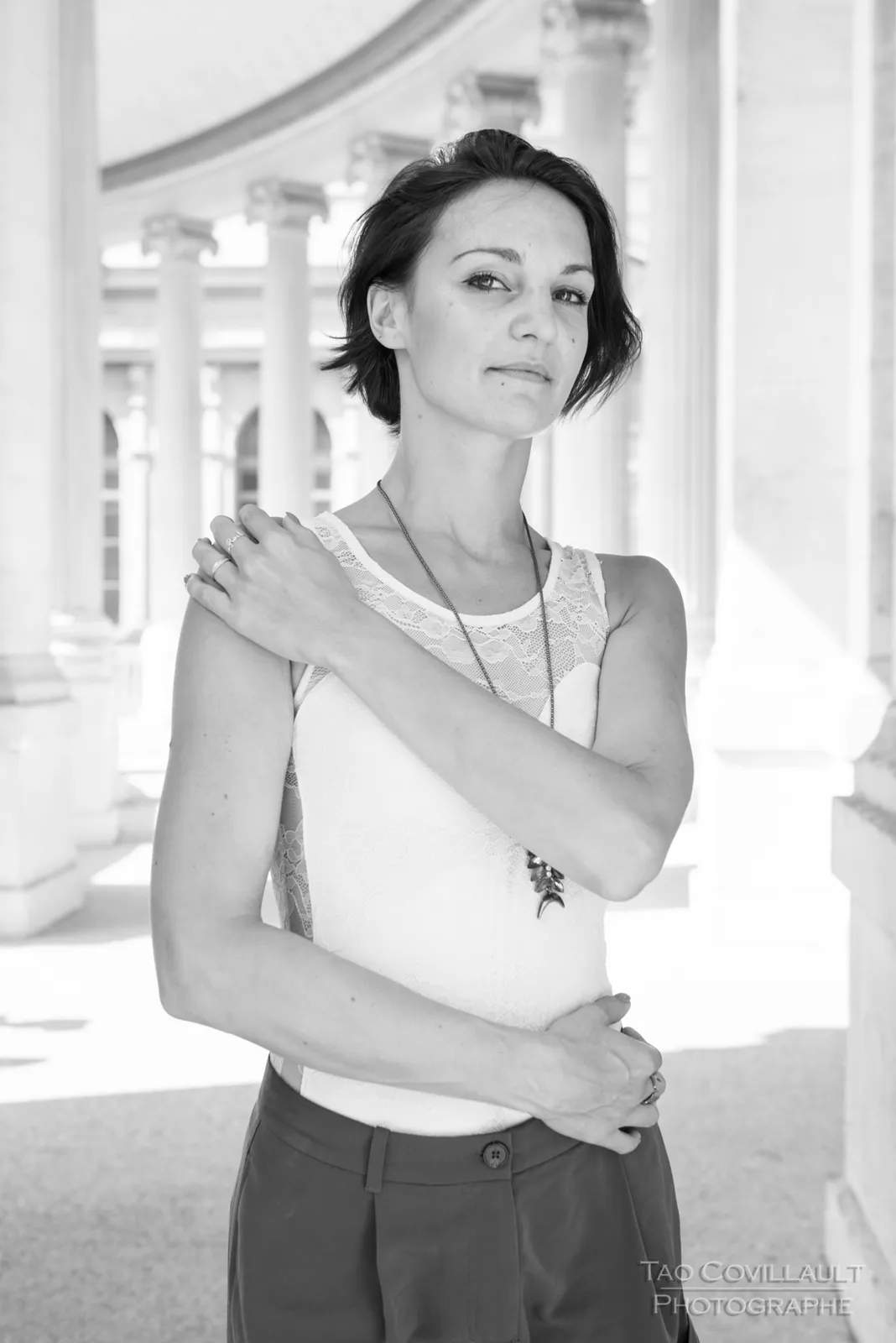 Black-and-white photograph: woman in a white sleeveless top posing beside pale stone columns.