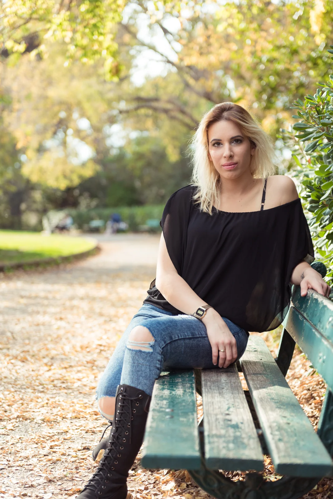 Woman in a black top and jeans seated on a green park bench.