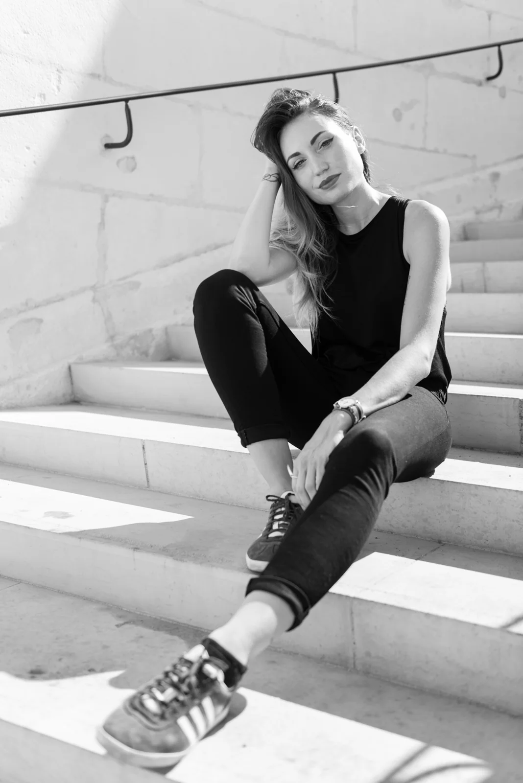 Black-and-white photograph: woman in black clothing posing on pale stone steps.
