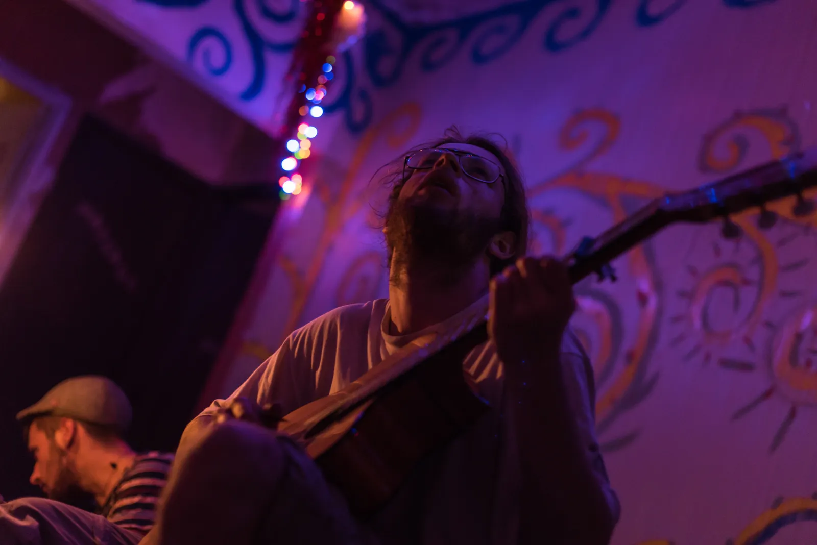 Musician playing a guitar under purple stage lighting.