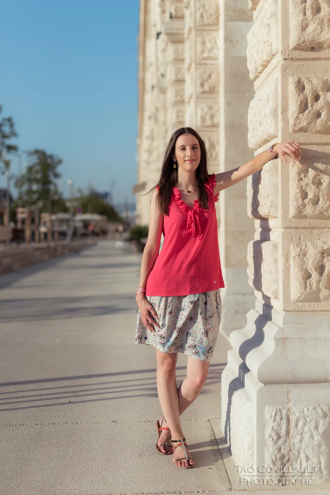 Woman in a bright pink top and patterned skirt posing beside stone steps and walls.