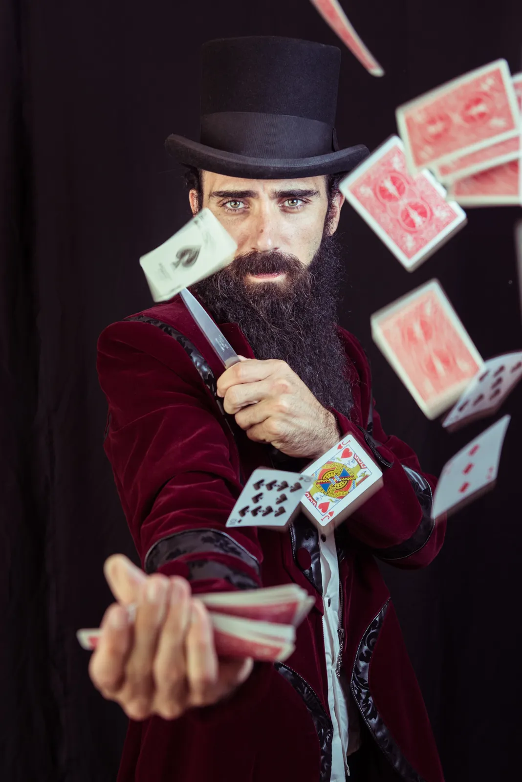Bearded performer in a top hat surrounded by playing cards.