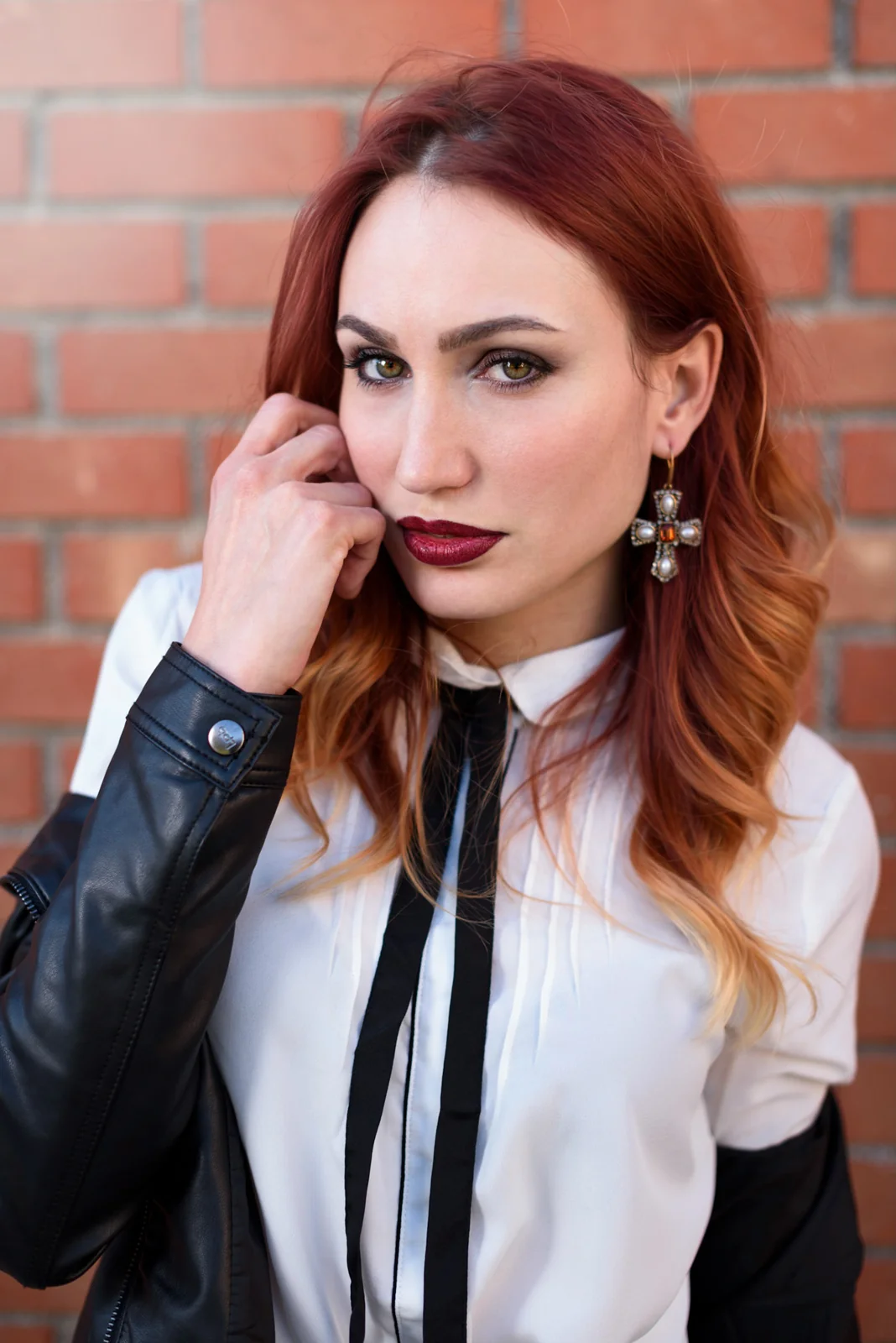 Red-haired woman standing against a brick wall.