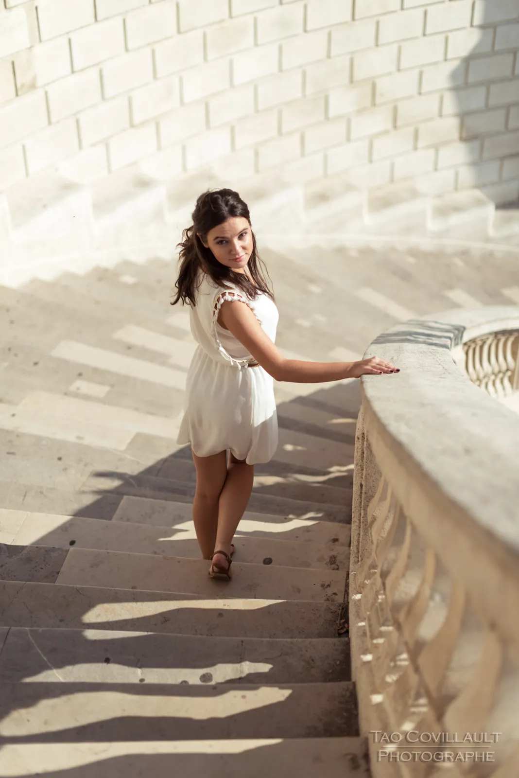 Woman in a white dress posing on stone steps and beside a balustrade.