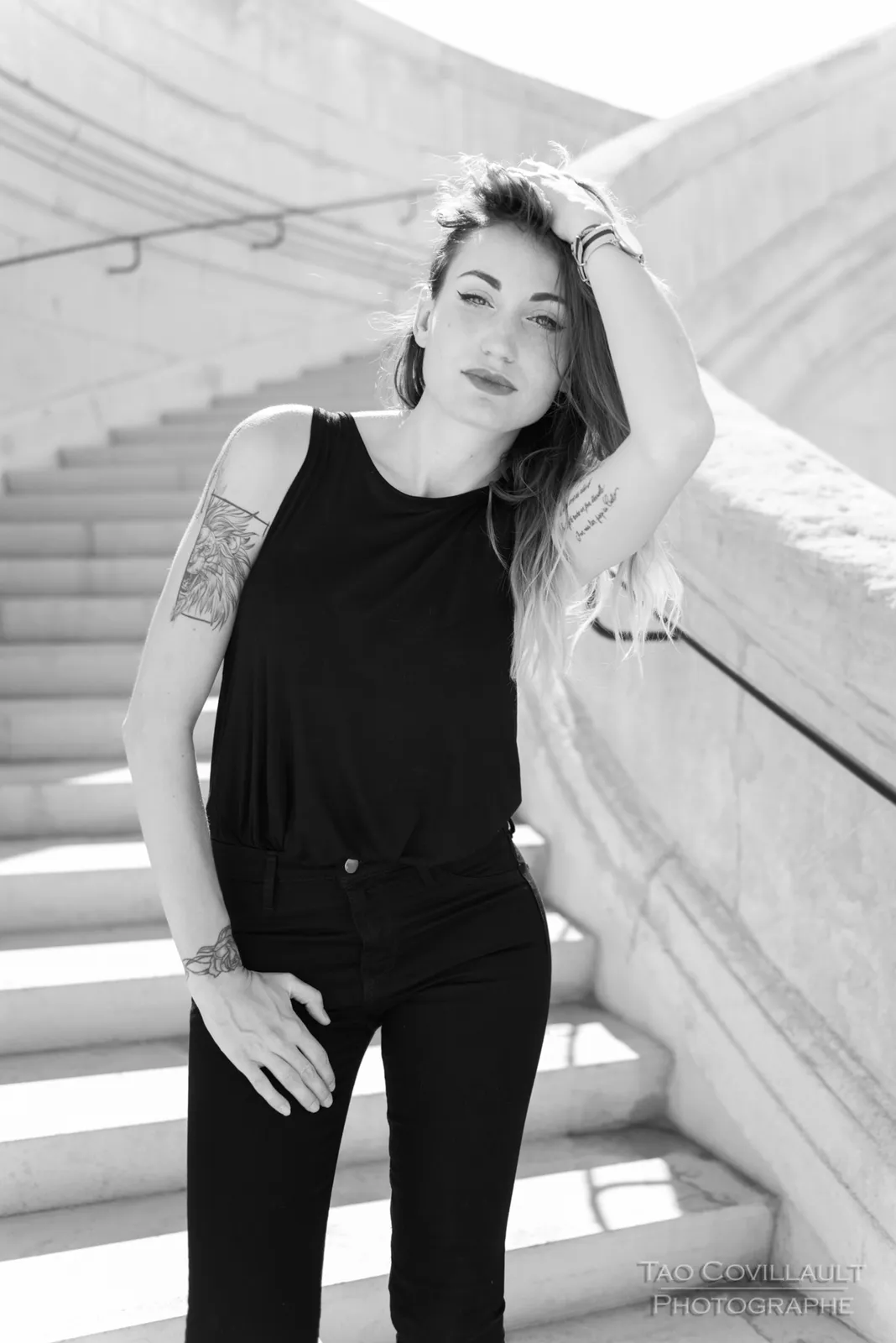 Black-and-white photograph: woman in black clothing posing on pale stone steps.