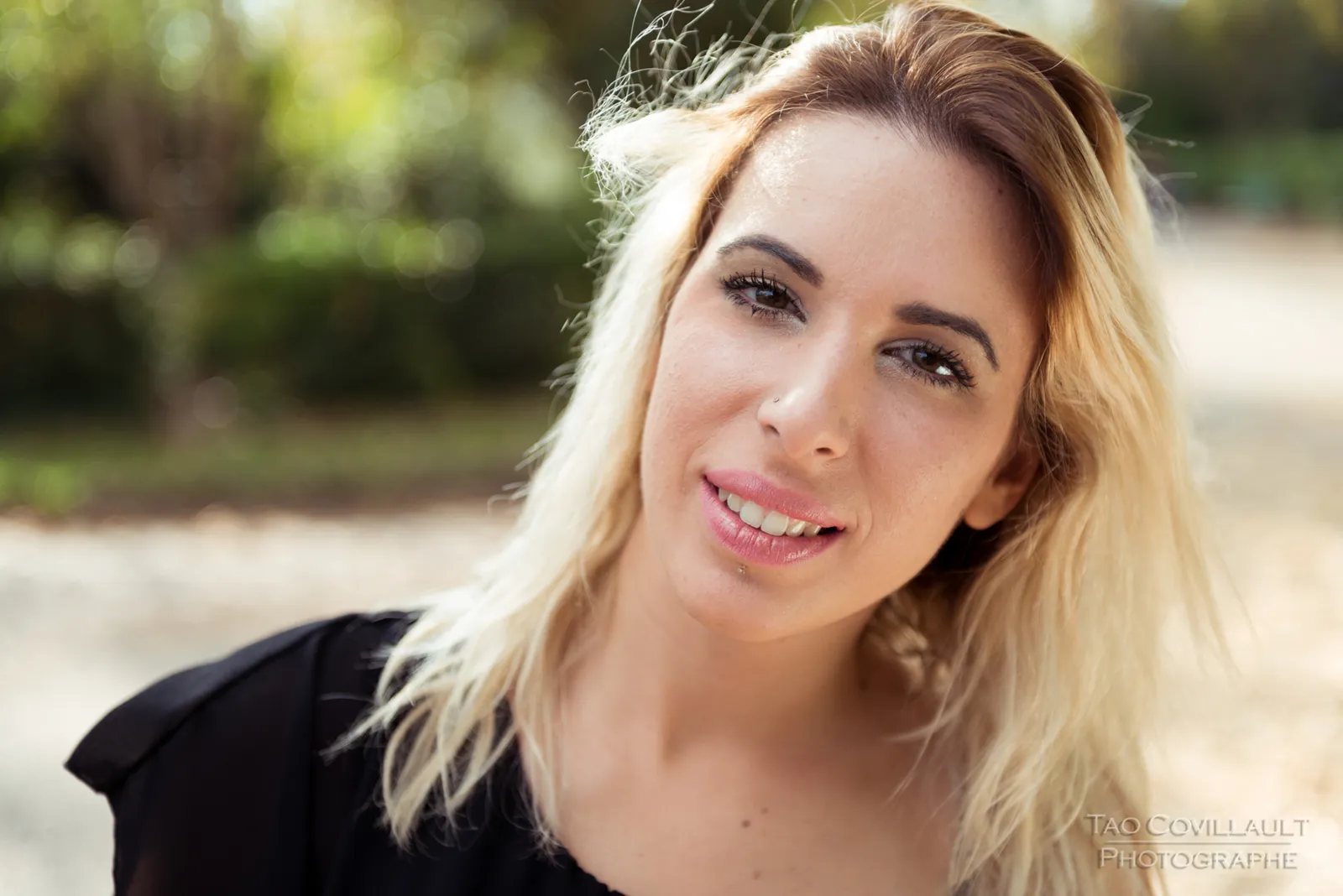 Woman in a black top and jeans posing in a leafy park.