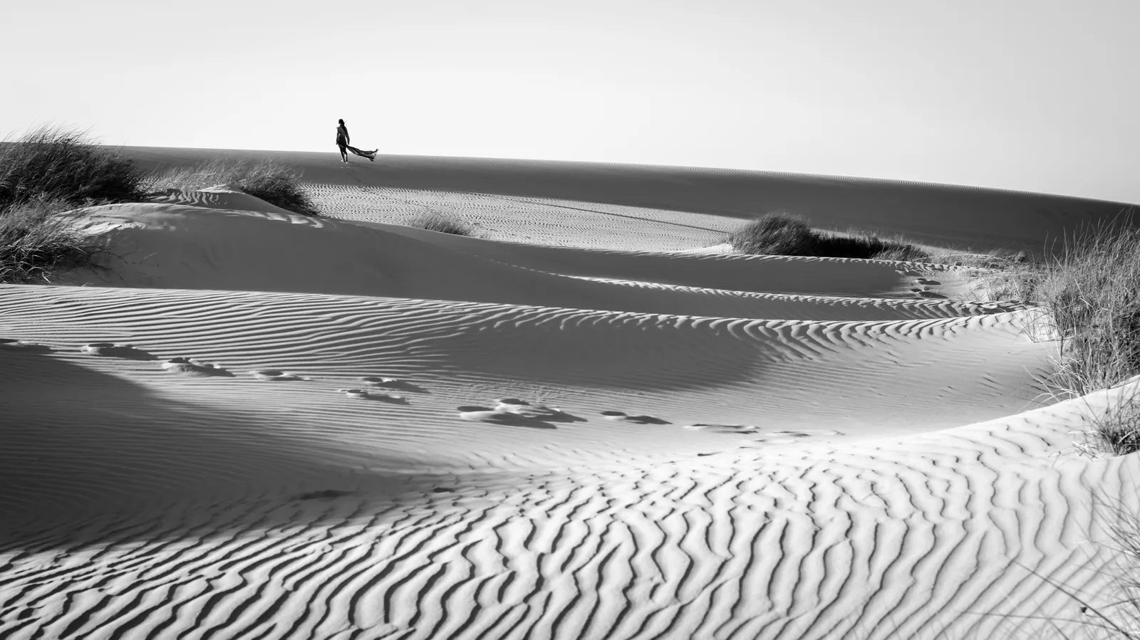 Lone figure crossing rippled sand dunes in black and white
