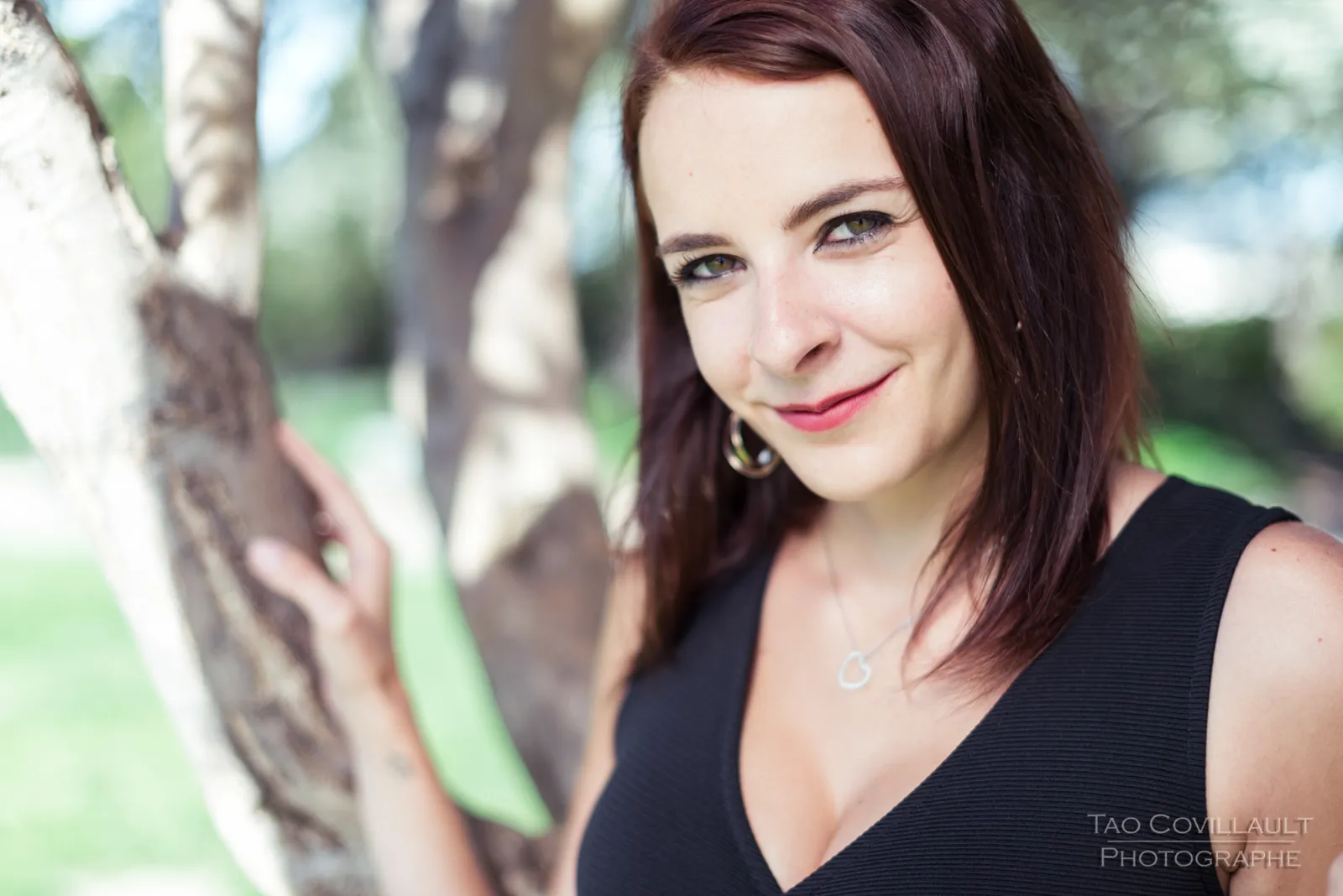 Woman in a black dress posing among trees.