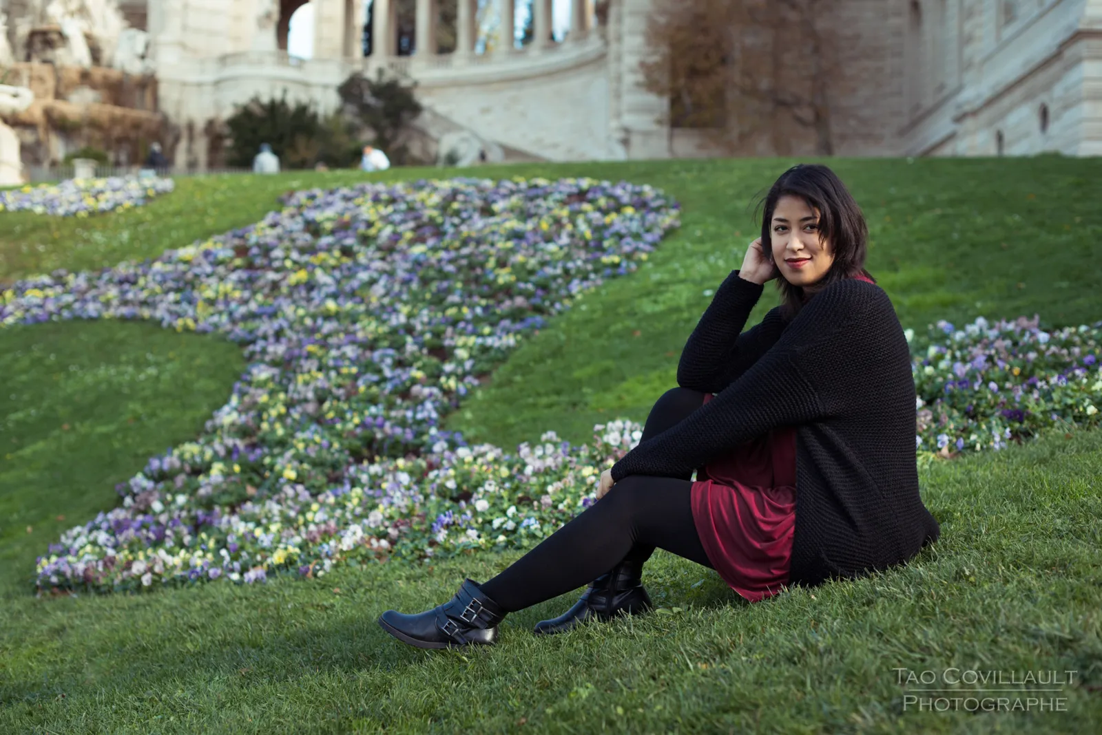 Woman in a burgundy dress relaxing on grass beside flowers.