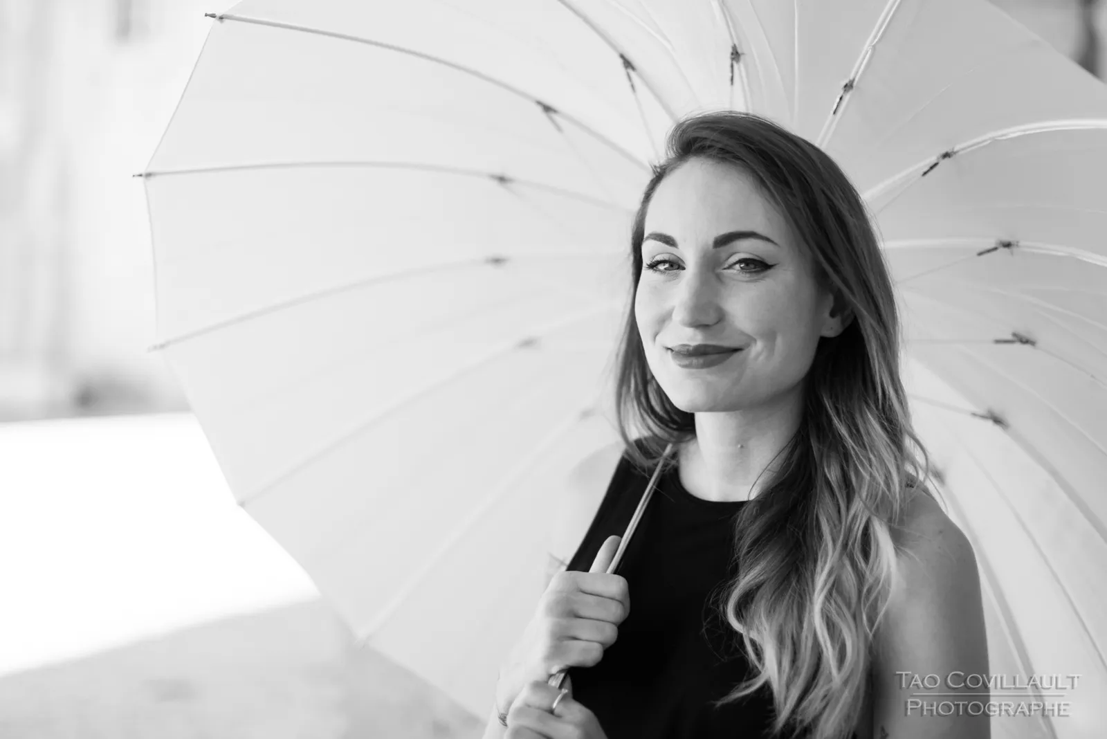 Black-and-white photograph: woman in black clothing holding a white parasol.