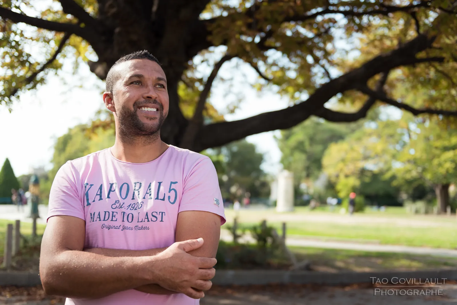 Man in a pink T-shirt standing beneath a tree.