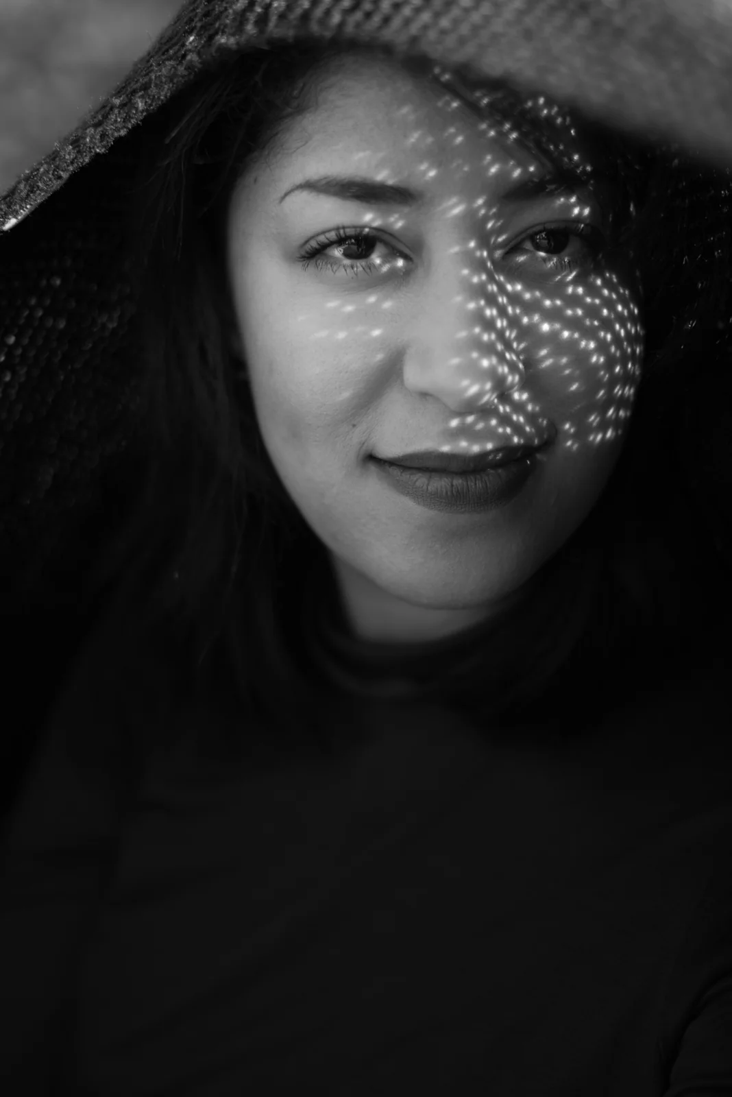 Black-and-white photograph: close-up portrait of a woman beneath a dark hood.
