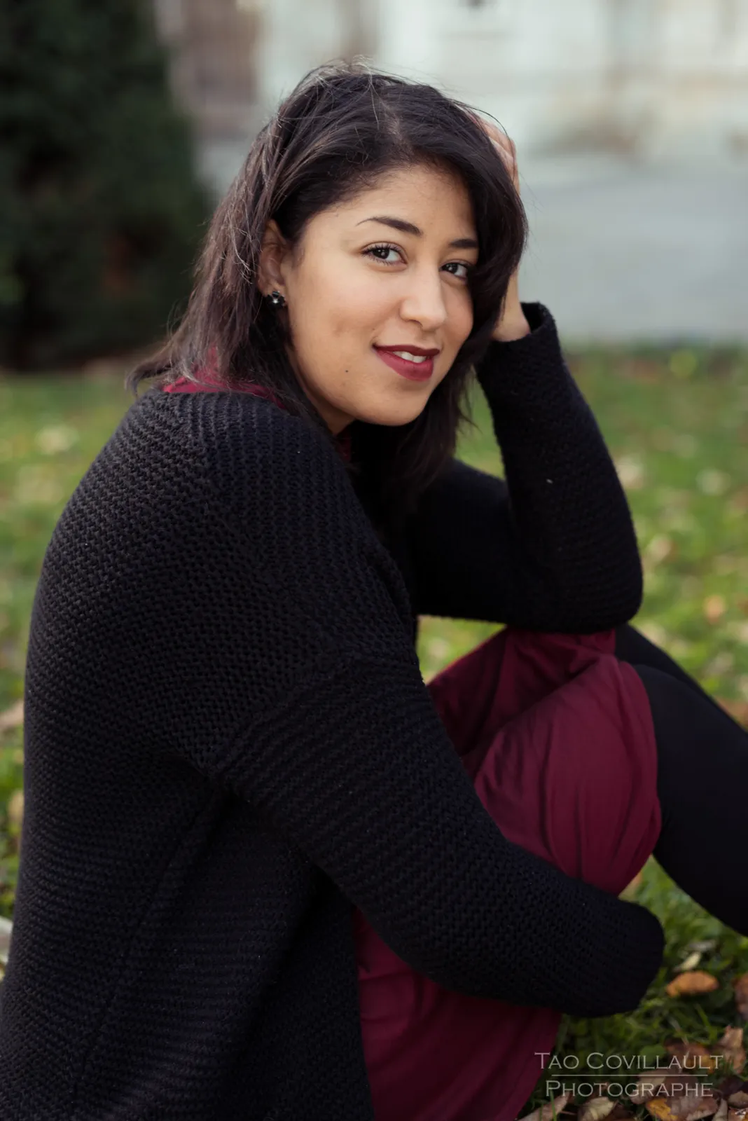 Woman in a burgundy dress and dark coat sitting among trees.