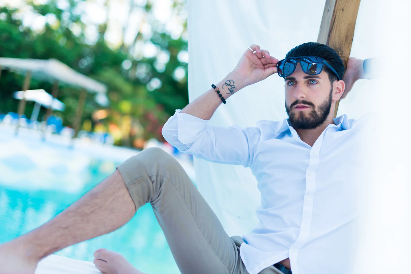 Man in a white shirt and cap reclining beside a swimming pool.