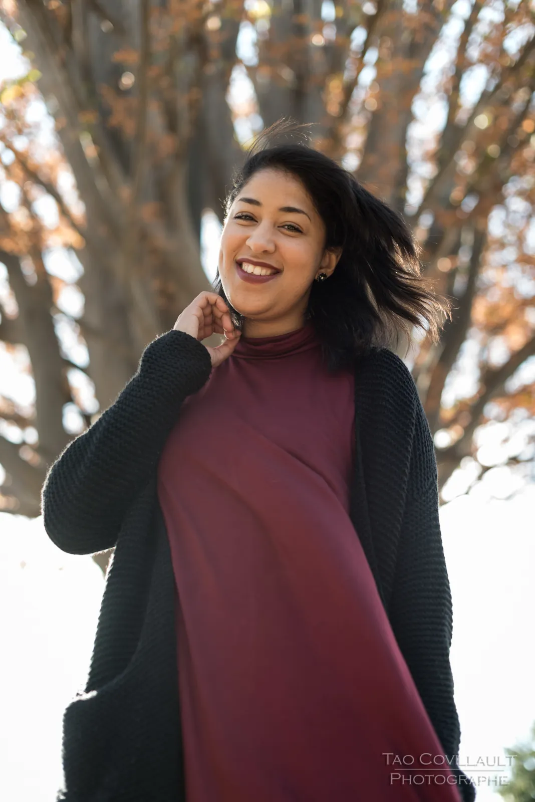 Woman in a burgundy dress standing beneath a tree.