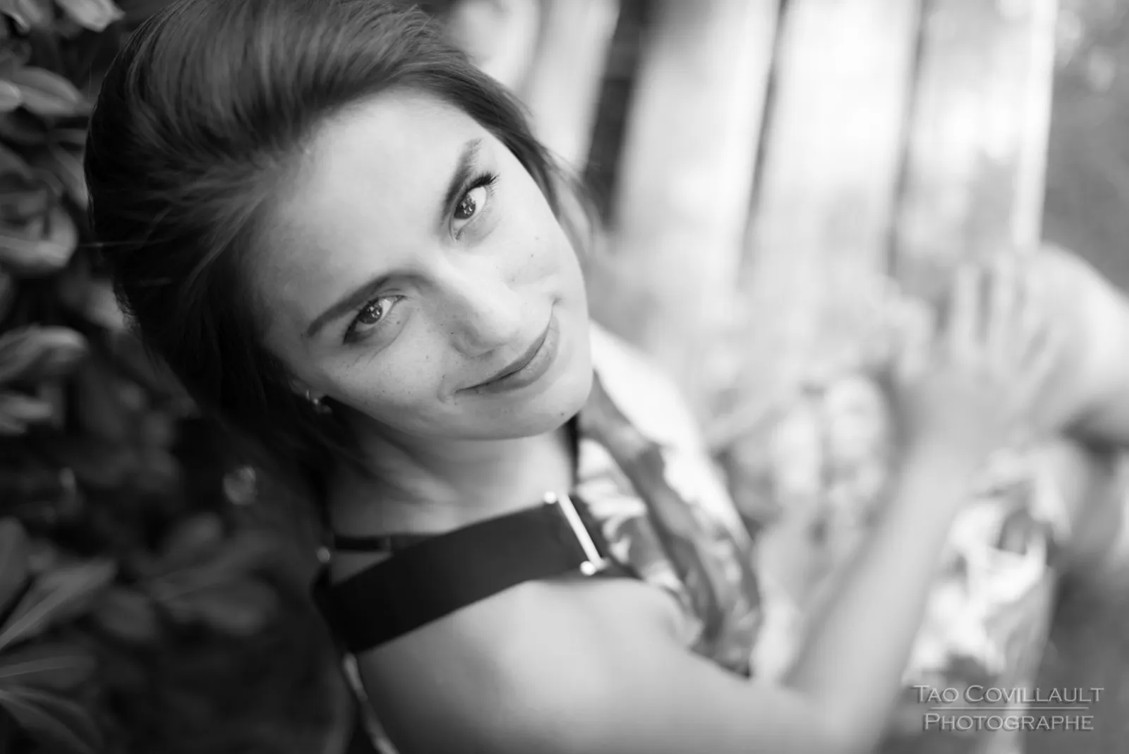 Black-and-white photograph: woman in a floral dress posing beside a green park bench.