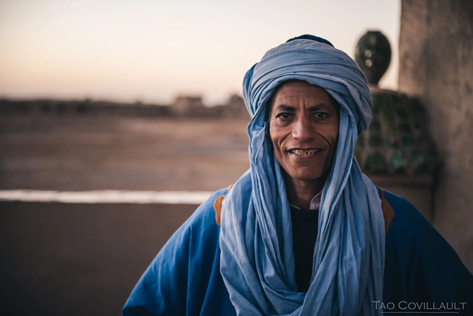 A man wearing a blue headscarf in a desert settlement.