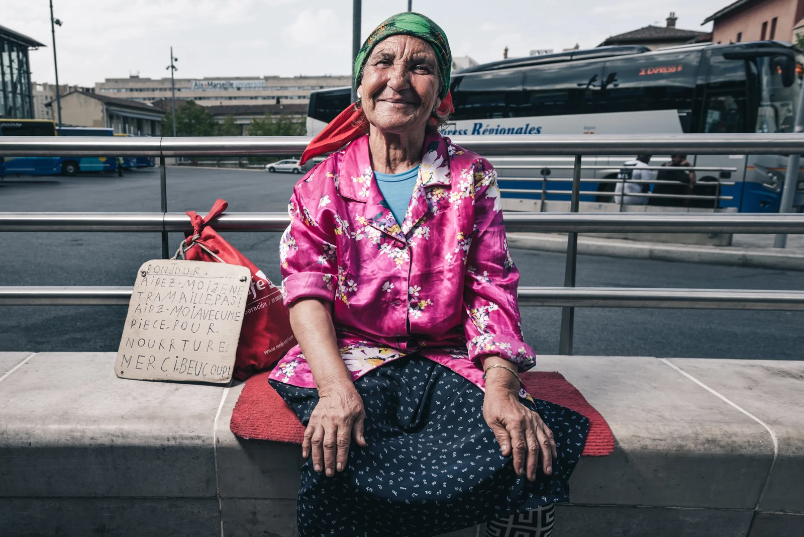 Woman in a pink jacket seated outside a railway station.