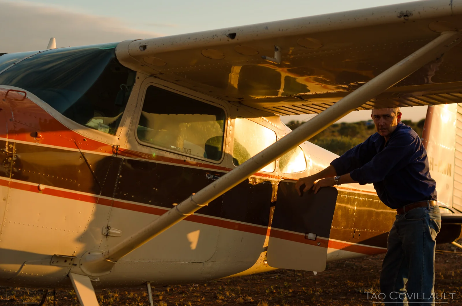 Man standing beside a small aircraft in warm evening light.